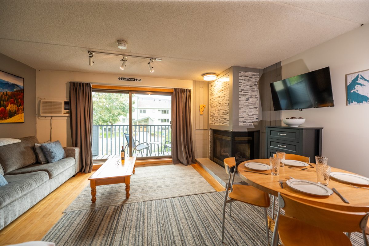Ski Stash Smuggs living area with sofa, corner gas fireplace, dining table and sliding glass door to the balcony