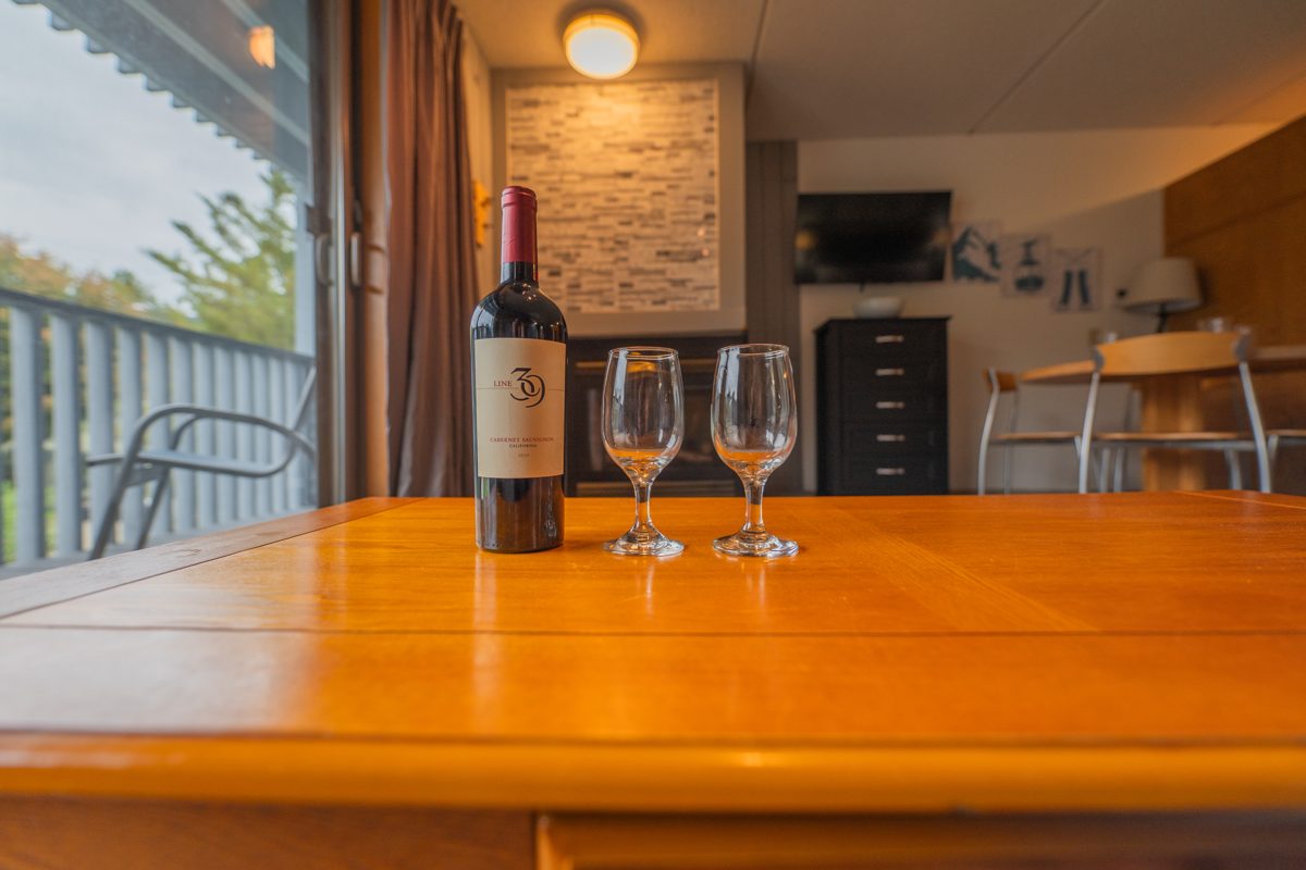 Bottle of wine and two glasses on the coffee table, with the gas fireplace softly blurred in the background